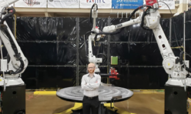 Justin Nussbaum standing in front of large-scale metal additive manufacturing machine