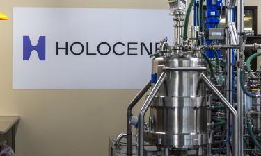 A sign on a wall reading "Holocene" in purple and black. The sign is displayed behind an industrial piece of equipment. 