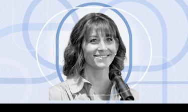 Black and white portrait of Megan O'Connor, smiling while speaking into a microphone. She has shoulder-length wavy hair and wears a light-colored blouse. The background is a light blue abstract pattern of interlocking circles.