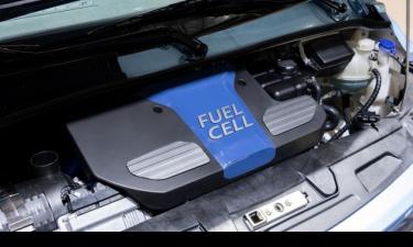 Close-up view of a hydrogen fuel cell system under the hood of a vehicle, with a prominent blue cover labeled "FUEL CELL" and surrounding engine components.
