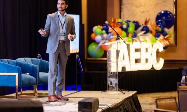 Speaker at the TAEBC (Tennessee Advanced Energy Business Council) Opportunities in Energy Conference presenting on stage with a colorful balloon arrangement and TAEBC signage in the background.
