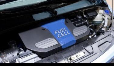 Close-up view of a hydrogen fuel cell system under the hood of a vehicle, with a prominent blue cover labeled "FUEL CELL" and surrounding engine components.