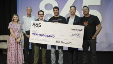 Group of six people standing on stage at 865 Fest 2025 holding an oversized check for $10,000 awarded to Witching Hour as the Judges’ Choice Prize Winner, presented by the Innov865 Alliance.